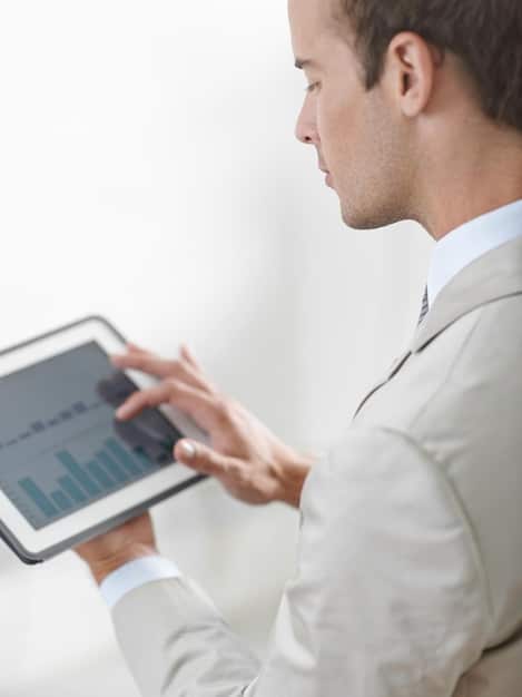 Close-up of a coach intensely reviewing a tablet displaying complex statistical data related to a Wild Rift match, highlighting key performance indicators and strategic insights. The coach's focused expression and the glow of the screen suggest a deep dive into data analysis.