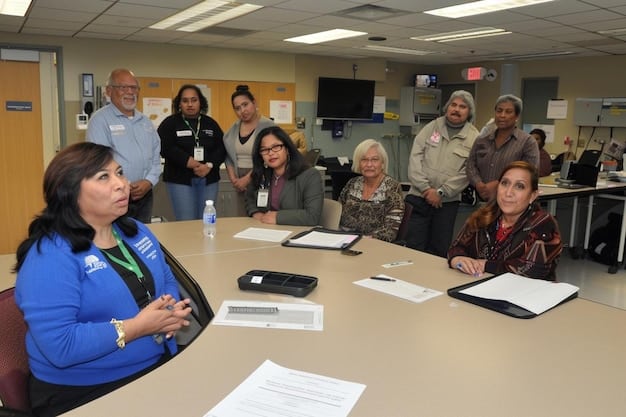 A diverse group of educators, administrators, and state officials gathered in a large conference room, intensely discussing policy documents and strategy maps, indicating a collaborative yet challenging process of educational reform.