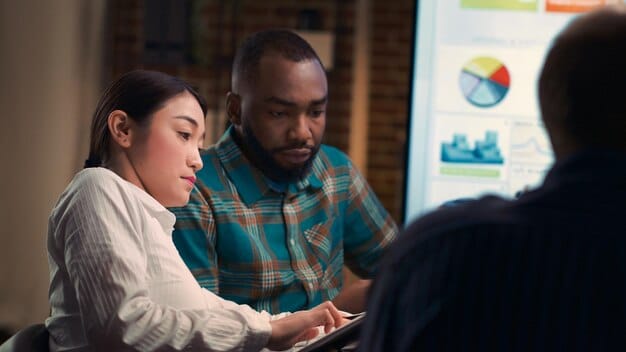 A diverse group of people, appearing concerned and engaged in conversation while looking at stock market charts on a computer screen, representing economic anxiety and financial news.