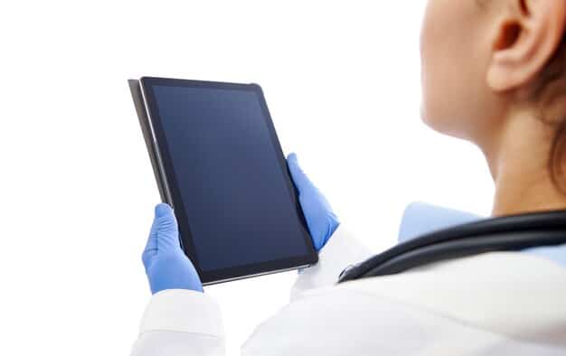 A close-up of a doctor's hand pointing at a tablet screen displaying an AI-generated heat map overlaid on a diagnostic image, highlighting potential anomalies. The background is a blurred hospital setting.