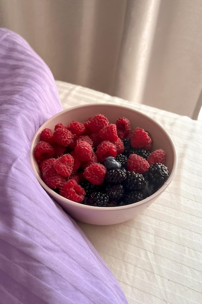 A close-up of a bowl filled with colorful berries (blueberries, raspberries, strawberries) with a few almonds scattered around, against a soft, bright background.