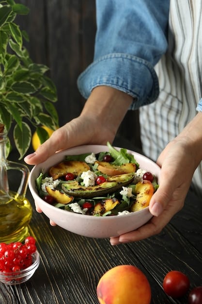A person's hands holding a vibrant, healthy salad bowl with a mix of leafy greens, colorful vegetables, grilled chicken, and a light dressing, suggesting a balanced meal.